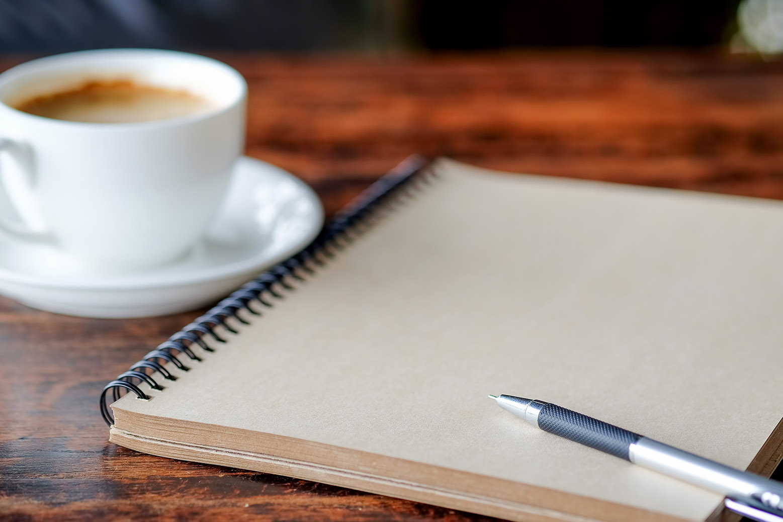 zdjęcie przedstawiające filiżankę kawy na spodku, obok notatnik z długopisem